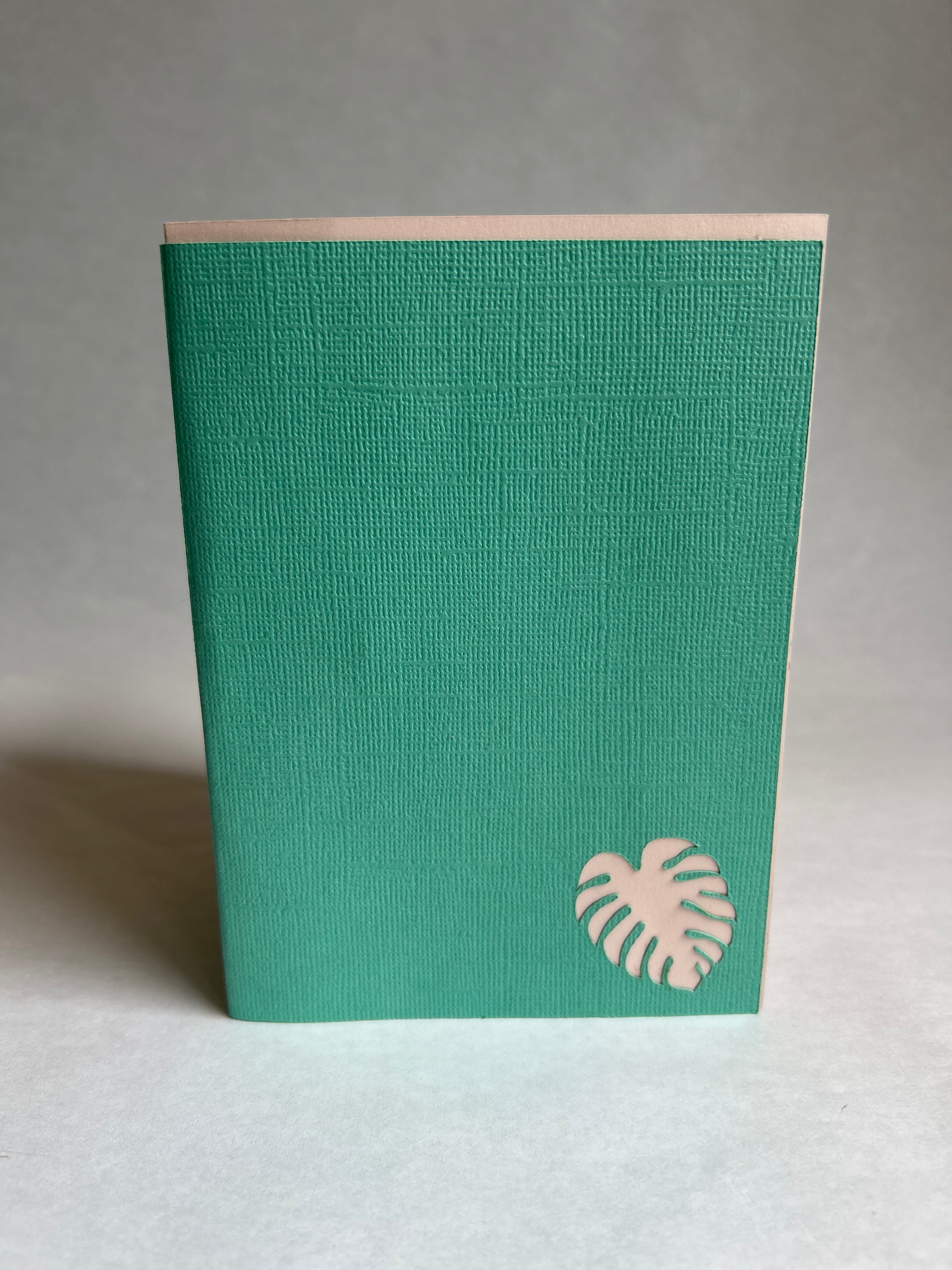 teal linen cover of greeting card with die cut pink monsterra 